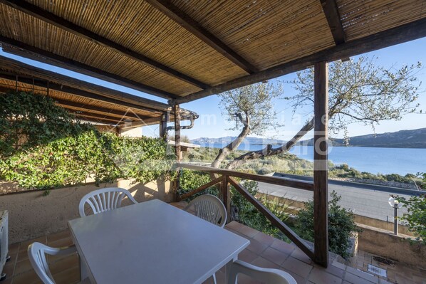 A covered outdoor seating area with a table and chairs, overlooking a body of water and hills.