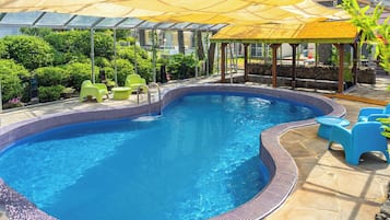 Piscina com borda azulejada, rodeada por vegetação e mobiliário de exterior.