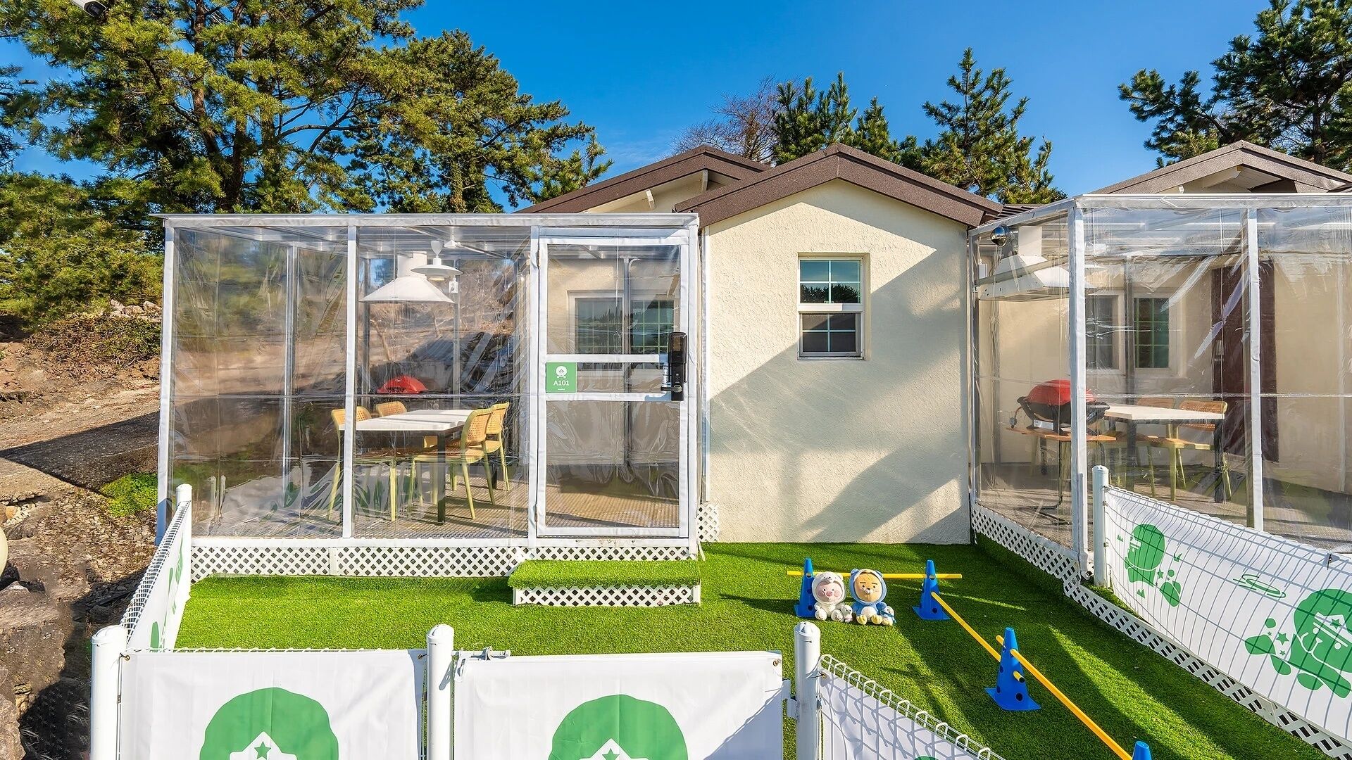 A house with a glass enclosure, a small deck, and a fenced area with a playset.