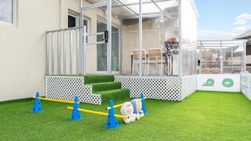 A children's play area with artificial grass, a climbing structure, and a covered seating area.