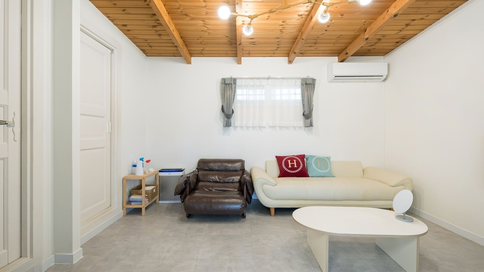 Una habitación con techo de madera, un sillón de cuero, un sofá, una mesita y una ventana con cortinas.