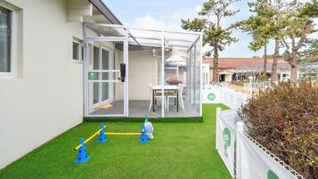 Un espacio al aire libre techado con puerta de vidrio, una mesa y sillas, y un área de juegos pequeña con conos y pelota.