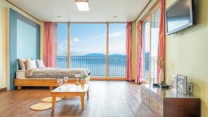 Un dormitorio con cama, mesita de noche y vistas al mar a través de amplias ventanas.