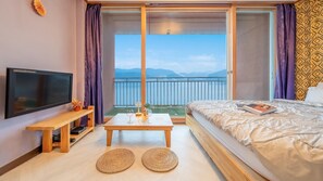 Habitación de hotel con cama, televisión, una mesita con vasos y vistas al mar desde un balcón.