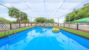 A rectangular swimming pool with a white canopy overhead, surrounded by a wooden deck and white lattice fencing. - Daebudo Green Beach Pension (Ansan)