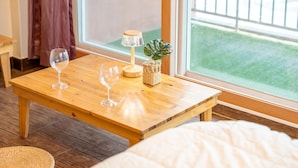 A wooden table with two wine glasses and a lamp, a woven basket, and a potted plant. - Daebudo Green Beach Pension (Ansan)