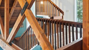 A wooden staircase with a metal handrail and a view of the outdoors through a window. - The Tower House | Hot Tub | Firepit | Dog-Friendly (Killington)