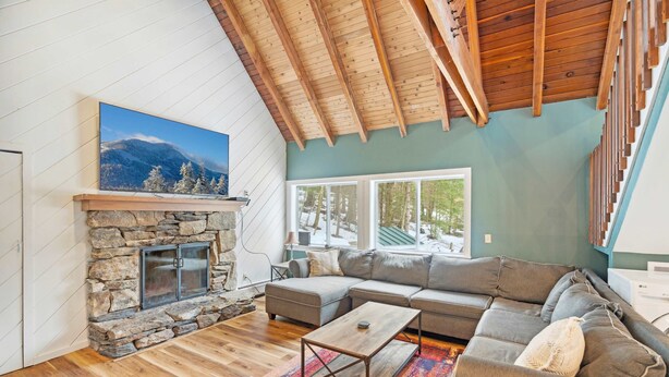 A cozy living room with a stone fireplace, a large sectional sofa, and a wooden ceiling. - The Tower House | Hot Tub | Firepit | Dog-Friendly (Killington)