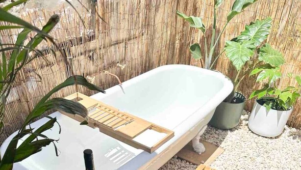 A spa area with a bathtub, a wooden stool with bottles, and potted plants. - Telegraph Station Stays

 (Penola)