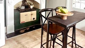 A dining area with a dark wooden table, two chairs, a hanging light fixture, a fireplace with a green wall, and a window with blinds. - Telegraph Station Stays

 (Penola)
