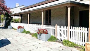 A residential building with a covered porch, white picket fence, and potted plants. - Telegraph Station Stays

 (Penola)