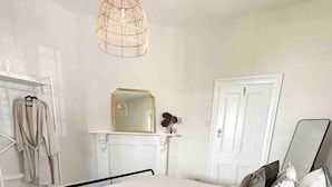 A bedroom with a bed, a bedside table, a mirror, a hanging light fixture, a coat rack, and a door. - Telegraph Station Stays

 (Penola)