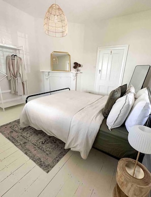 Quarto com cama, mesa de cabeceira, espelho, luminária pendente, cabideiro e porta.