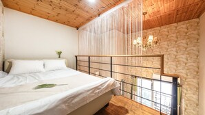 Un dormitorio con techo de madera, una cama con ropa de cama blanca, una planta decorativa y una ventana con vistas.
