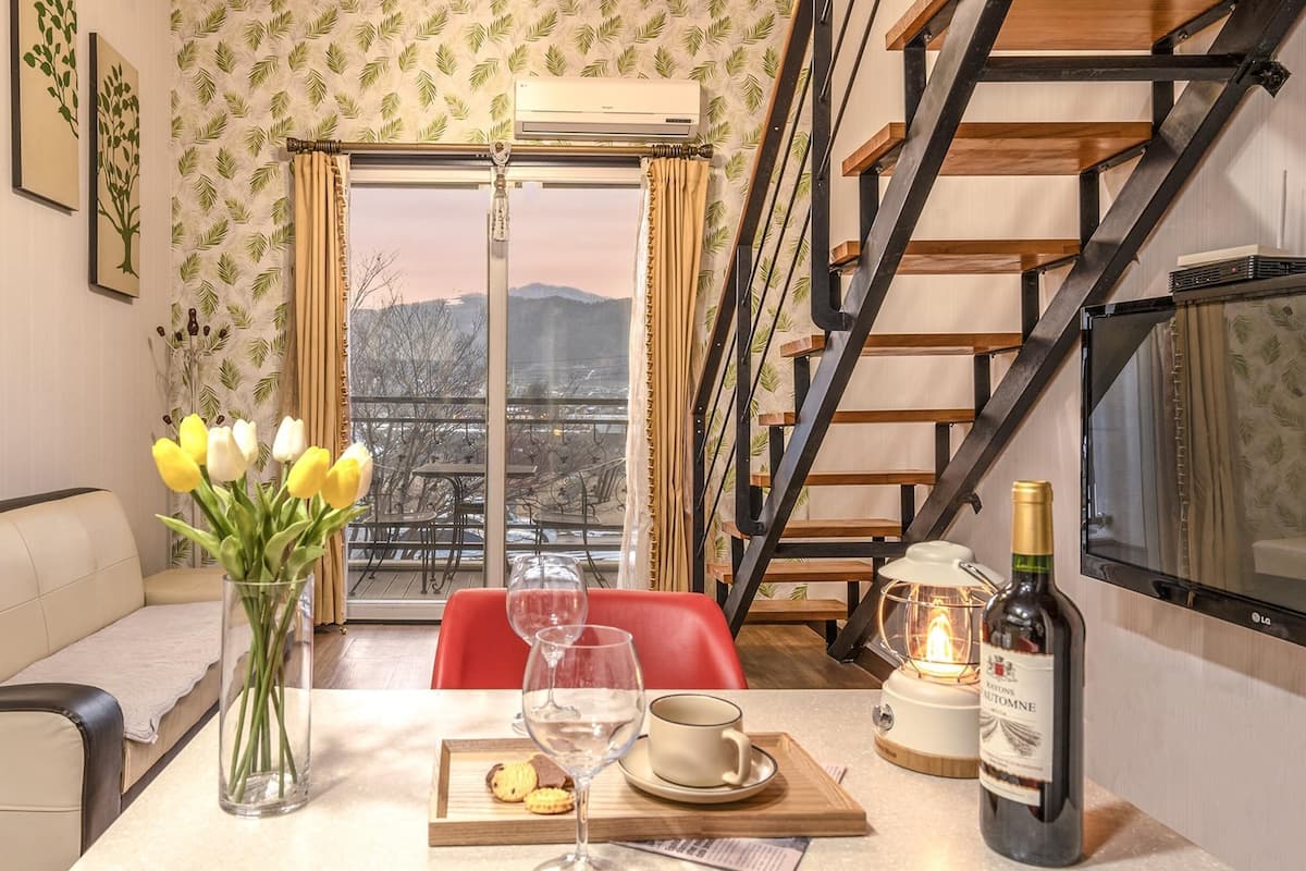Ein Essbereich mit einem für zwei gedeckten Tisch, einer Vase mit gelben Tulpen, einer Weinflasche und einer Kerze auf einem Balkon mit Blick auf eine Stadtlandschaft.