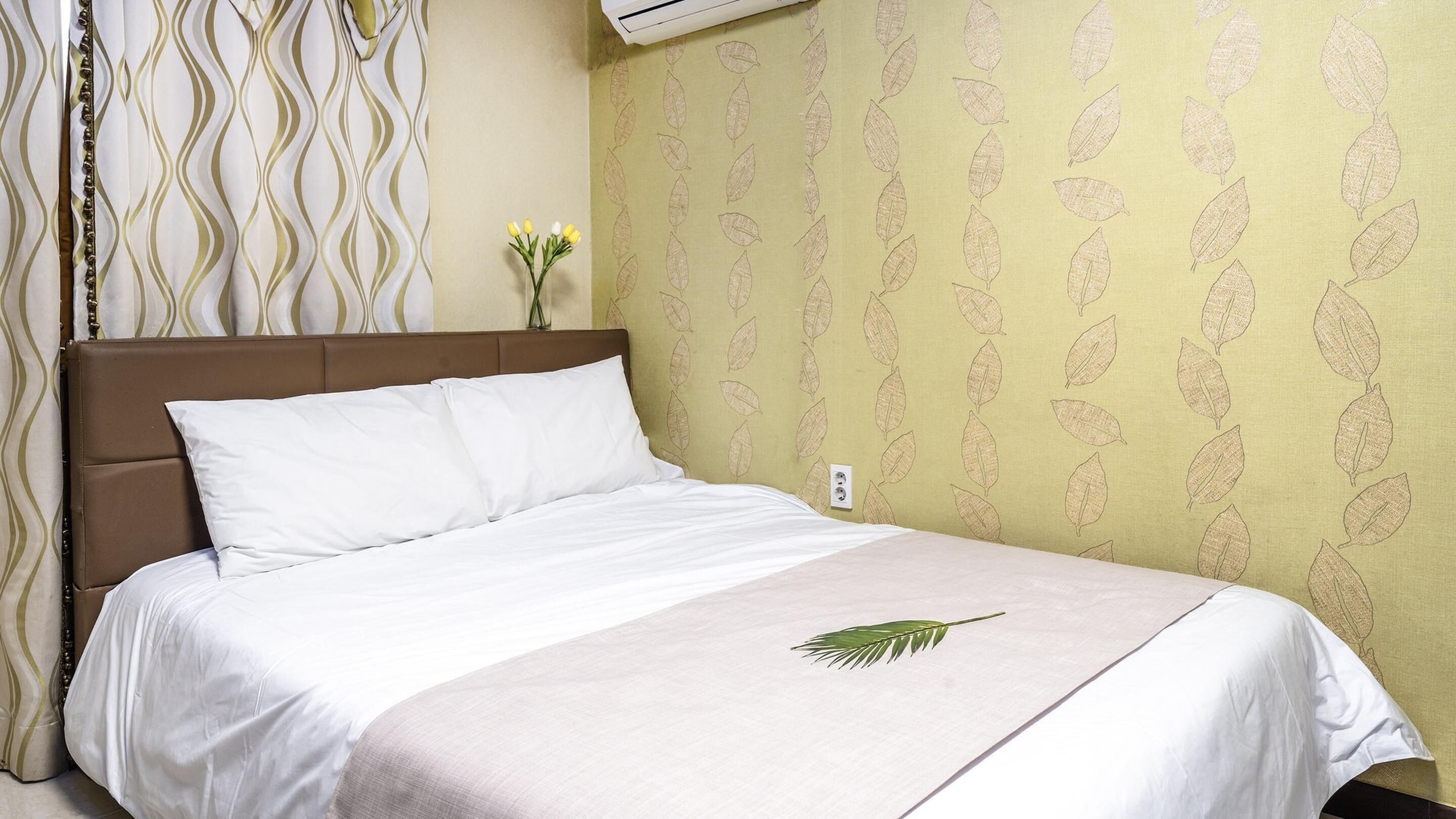 Une chambre d’hôtel avec un lit, un mur orné d’un motif de feuilles et une fenêtre avec des rideaux.