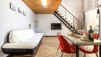 Una sala de estar moderna con un sofá blanco, sillas rojas, una escalera de madera y una mesa de comedor con una botella de vino.