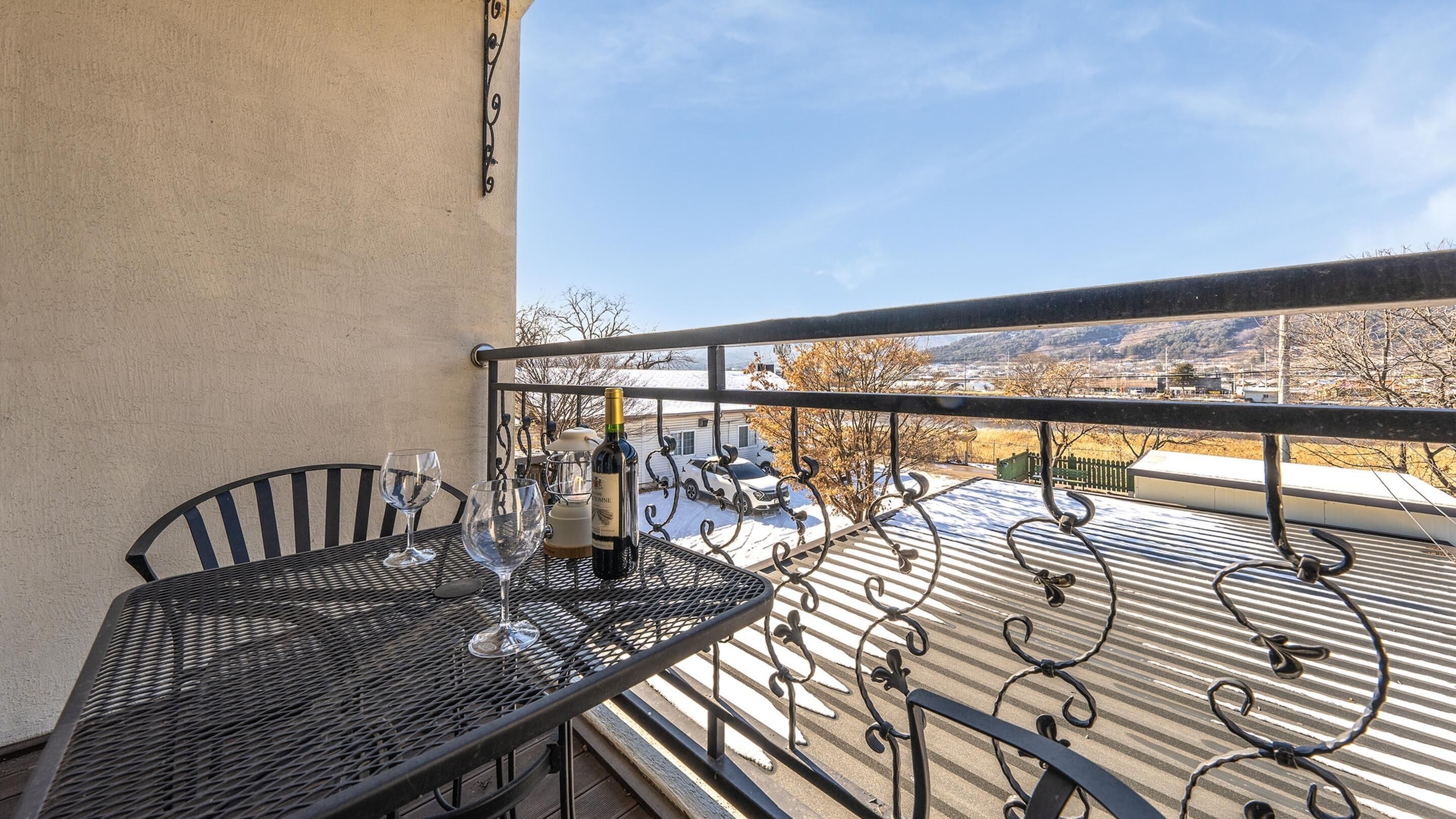 Un balcon avec une table et des chaises en métal, une bouteille de vin et un verre.