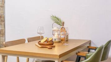 A wooden dining table with a bowl of bread, a wine glass, a candle, and a bottle of wine.