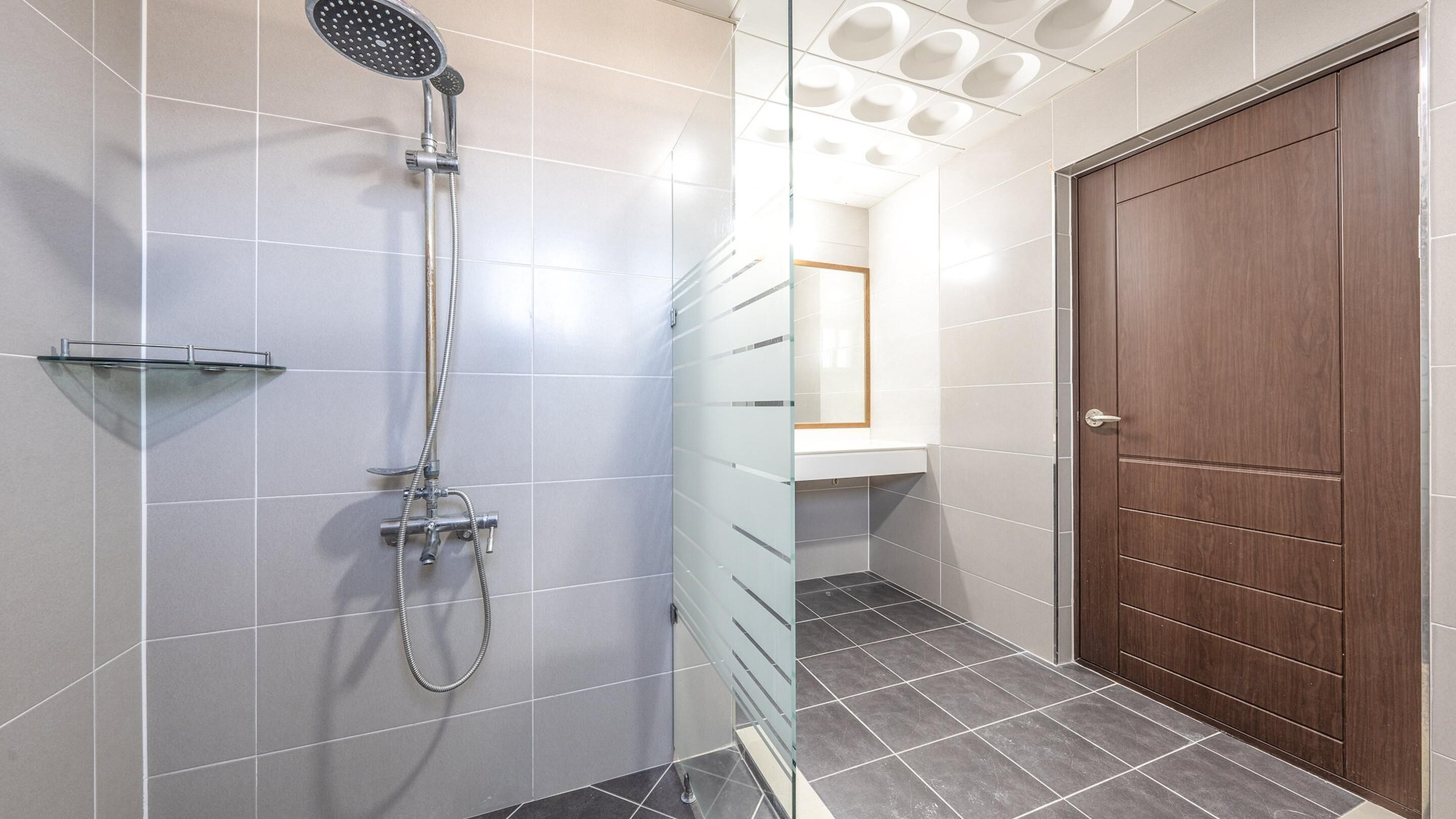 A modern bathroom with a glass shower enclosure, a wooden door, and a tiled floor.