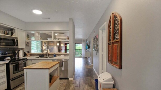A modern kitchen with white cabinetry, a central island, stainless steel appliances, and a wooden floor.