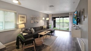 A modern living room with a sectional sofa, a coffee table, and a TV mounted on the wall.
