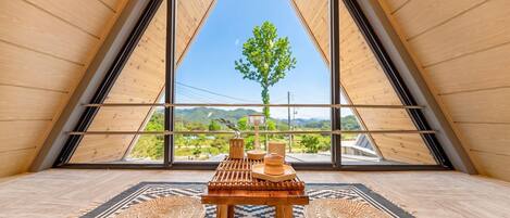 Una habitación con techo inclinado, una mesa con lámpara y vistas a un árbol y paisaje.