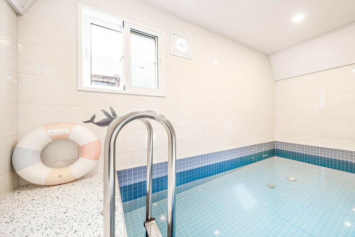 A swimming pool with a blue tiled border, a metal ladder, and a lifebuoy against the wall.