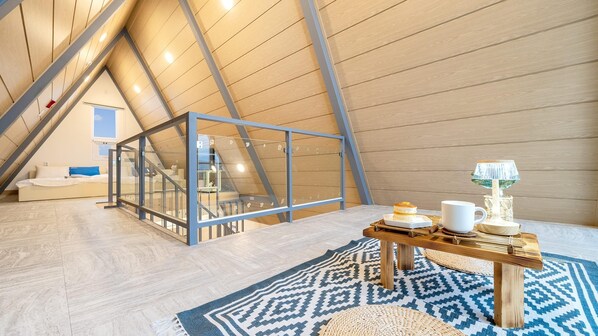 A modern loft bedroom with a sloped ceiling, a glass partition, a bed, a small table with a lamp, and a patterned rug. - Gapyeong The Paran Private Pool Villa (Gapyeong)