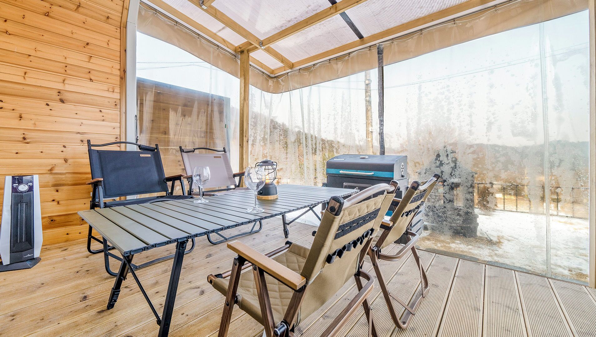En inredd miljö med träpanel, ett bord, stolar, en grill och utsikt över det fria.