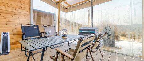 En inredd miljö med träpanel, ett bord, stolar, en grill och utsikt över det fria.