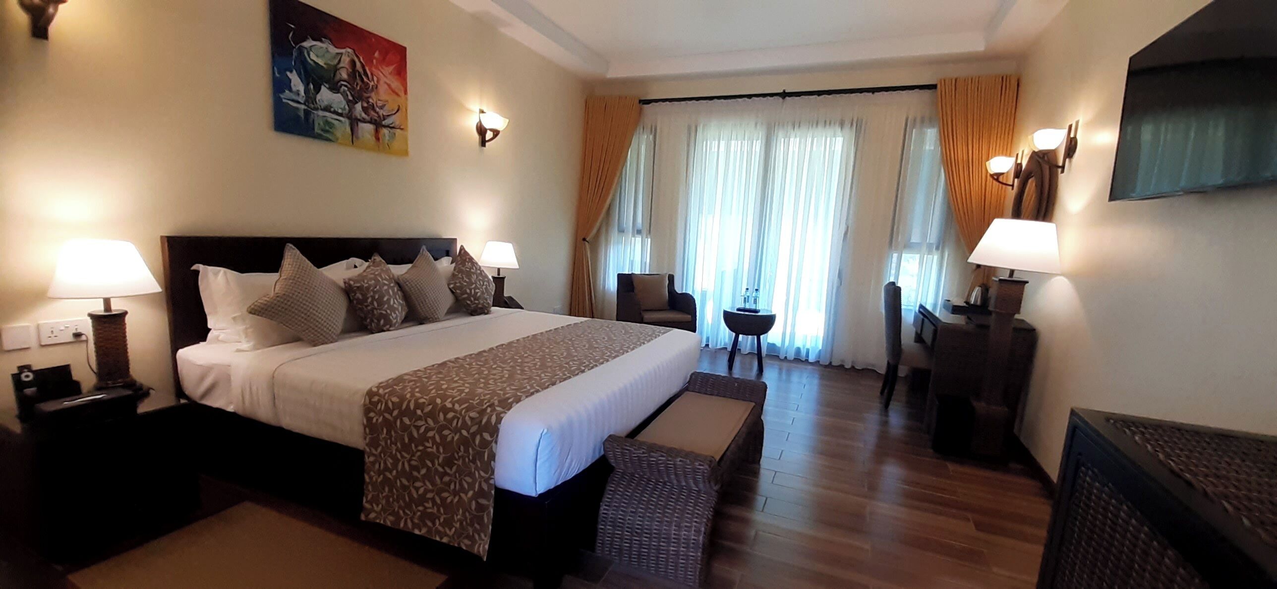 A hotel room with a large bed, two bedside tables, a small side table, a sofa, a TV, and a window with curtains.