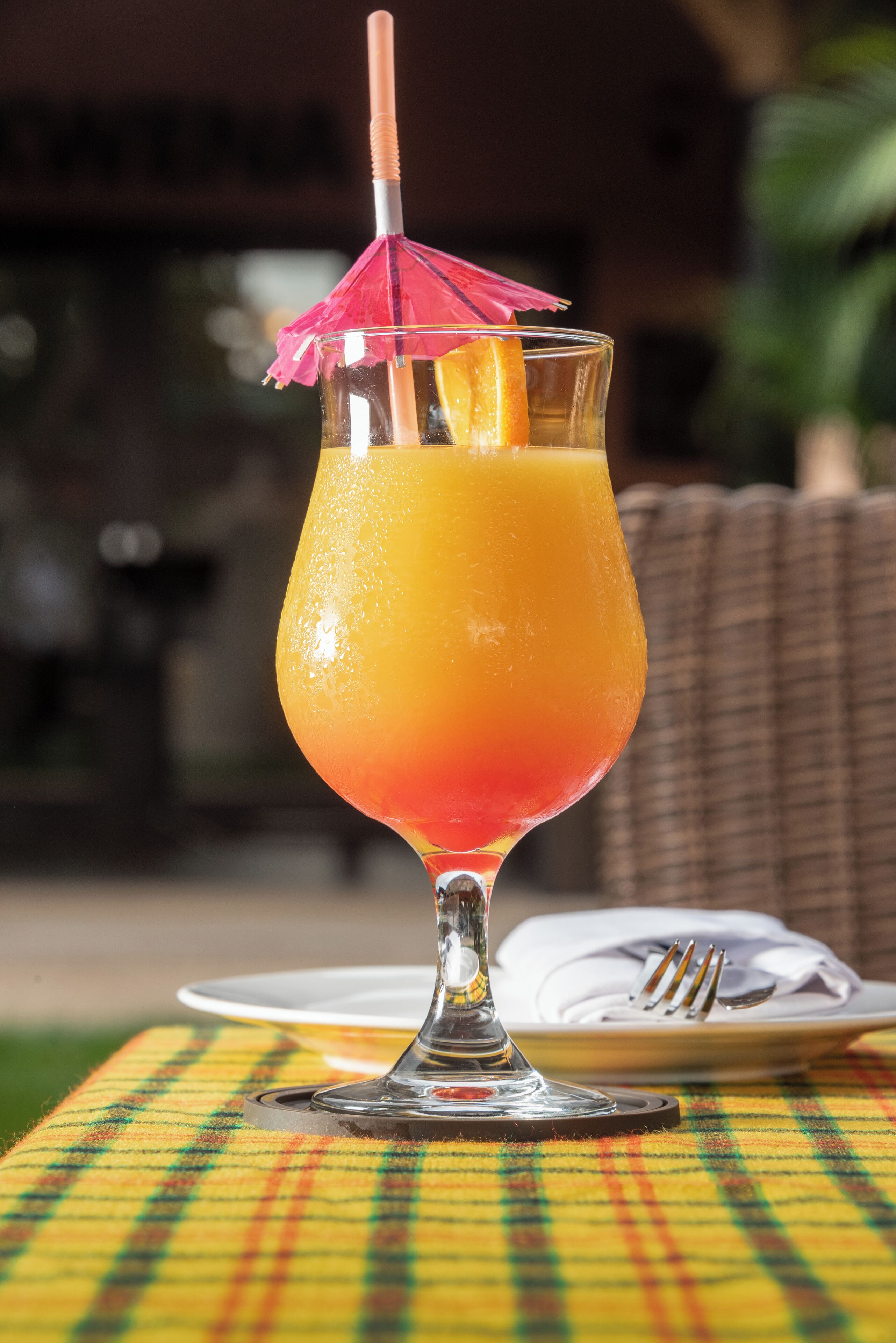 A glass of orange juice with a straw and a pink umbrella on a tablecloth.