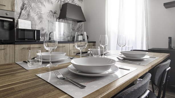A modern dining area with a wooden table set for four, including white plates and wine glasses. - Italianway Comfort - Buenos Aires 65 E (Milan)