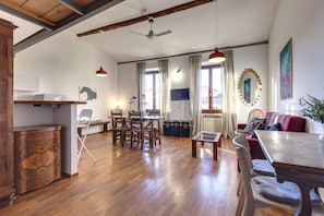 Een ruime woonkamer met houten vloer, een eettafel, een bank en een televisie.