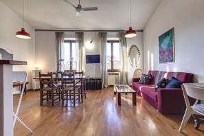 Een woonkamer met een rode bank, houten vloer, een eettafel met stoelen, een televisie en een plafondventilator.