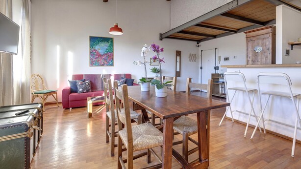 Un coin repas avec une table et des chaises en bois, un canapé rouge et un tableau accroché au mur.