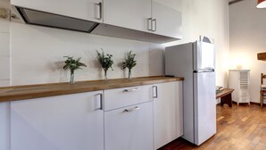 Une cuisine avec des armoires blanches, un plan de travail en bois et un réfrigérateur. On y trouve trois petites plantes en pot, disposées sur le plan de travail.
