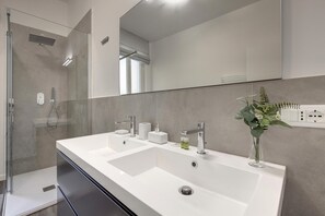 Une salle de bain moderne avec un grand lavabo blanc, une cabine de douche en verre et un miroir au-dessus du lavabo.