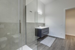Une salle de bain moderne avec une douche à l’italienne en verre, un meuble-lavabo foncé et un grand miroir.