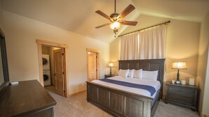 A bedroom with a wooden bed, a ceiling fan, a nightstand with a lamp, and a washing machine in the adjacent room. - Frey Gulch 46 (Keystone)