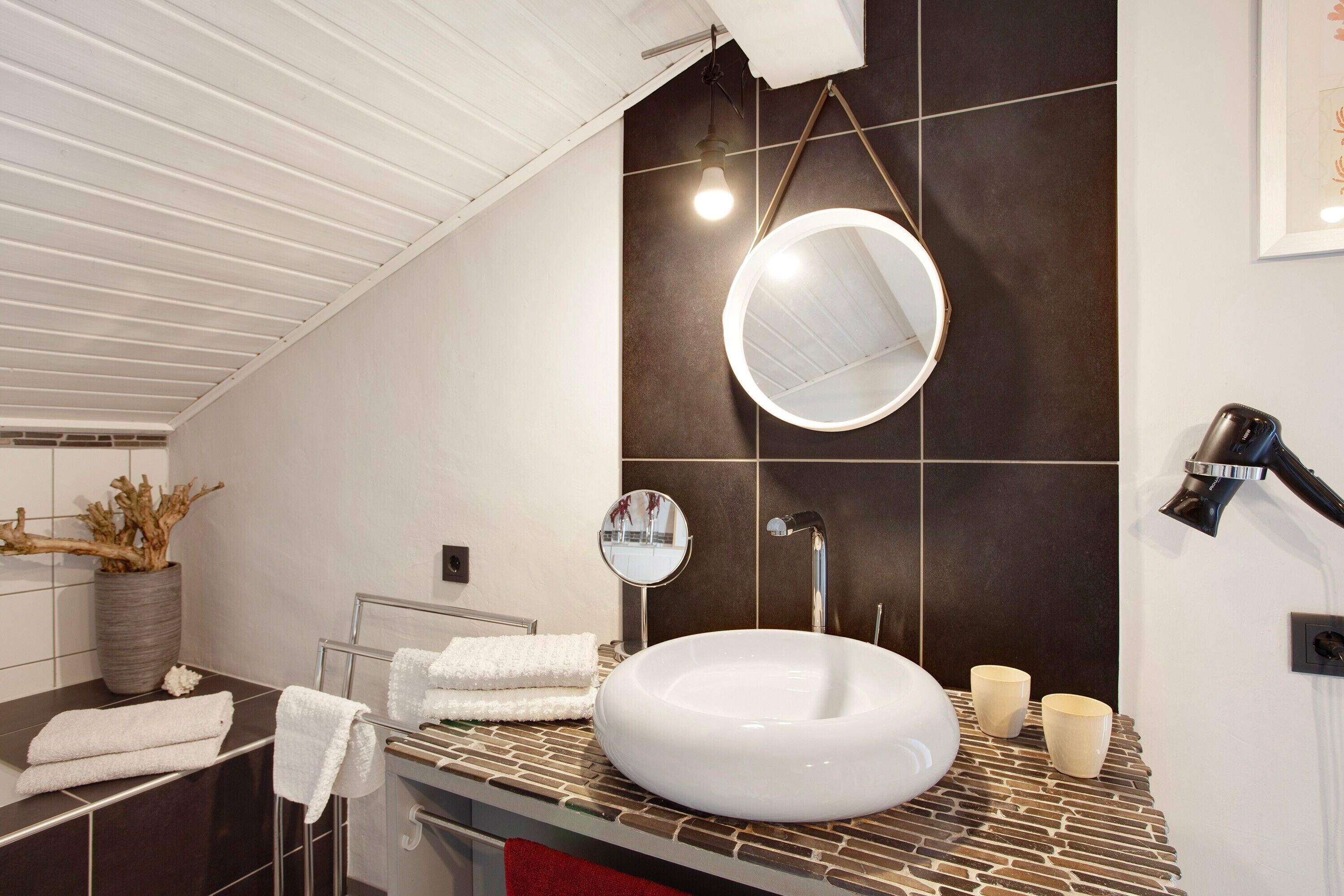 Ein modernes Badezimmer mit einem weißen Waschbecken, zwei Spiegeln, einem Fön und einem Handtuchhalter.