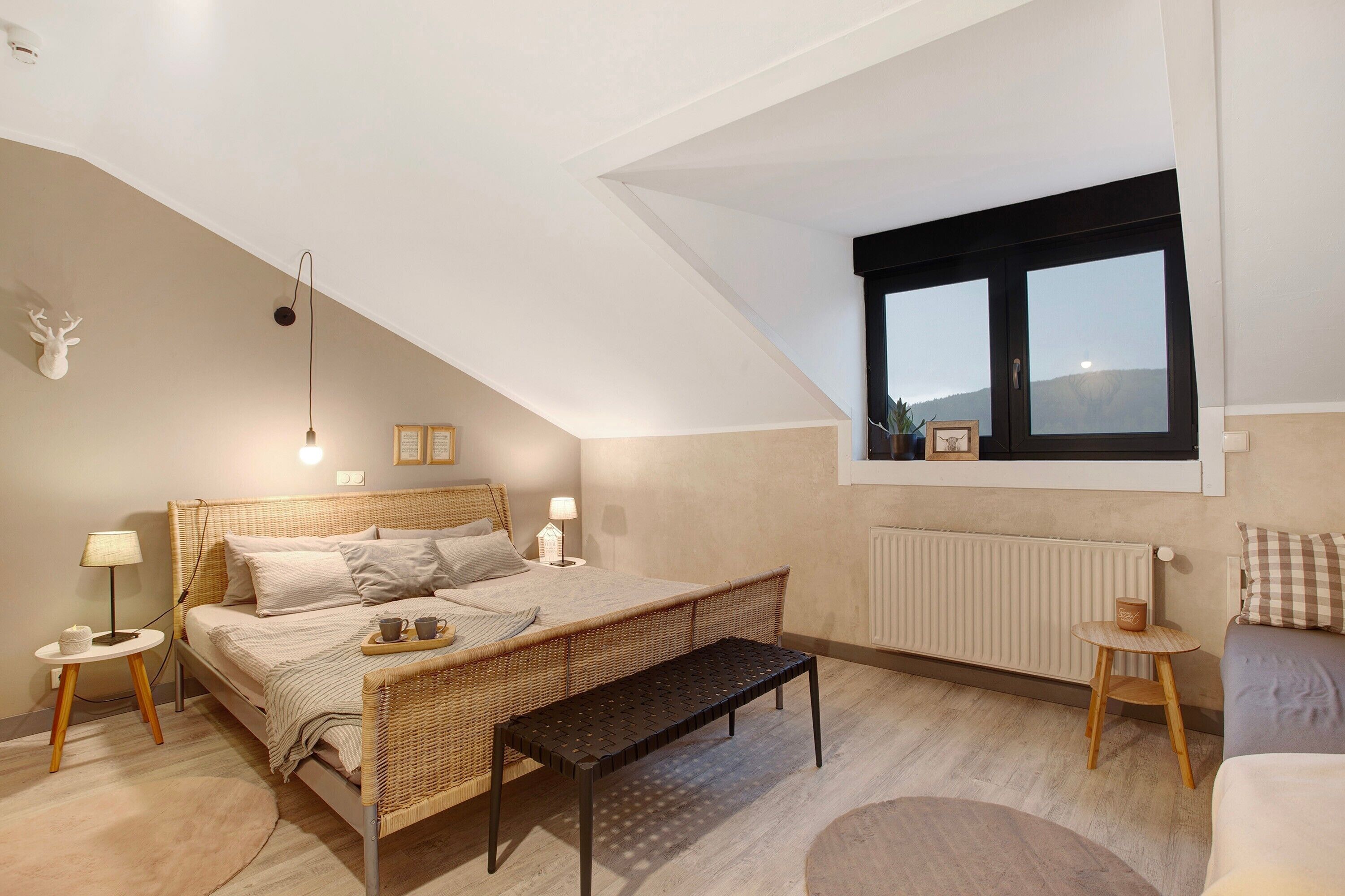Ein Schlafzimmer mit Bett, Nachttischen, einer Bank, einem Fenster und einem Heizkörper.