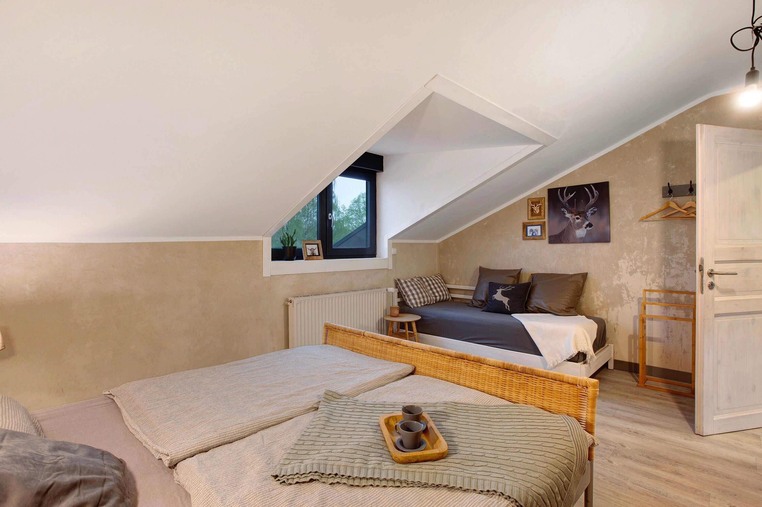 Une chambre avec un plafond en pente, un lit avec une tête de lit, une fenêtre et une petite table avec un plateau.