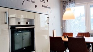 Et moderne køkken med indbygget ovn, spiseområde med bord og stole, samt en væg med tekst om kaffe.