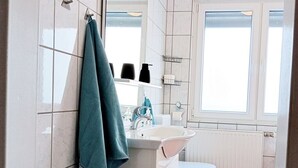 Et badeværelse med en hvid vask, toilet og et vindue.