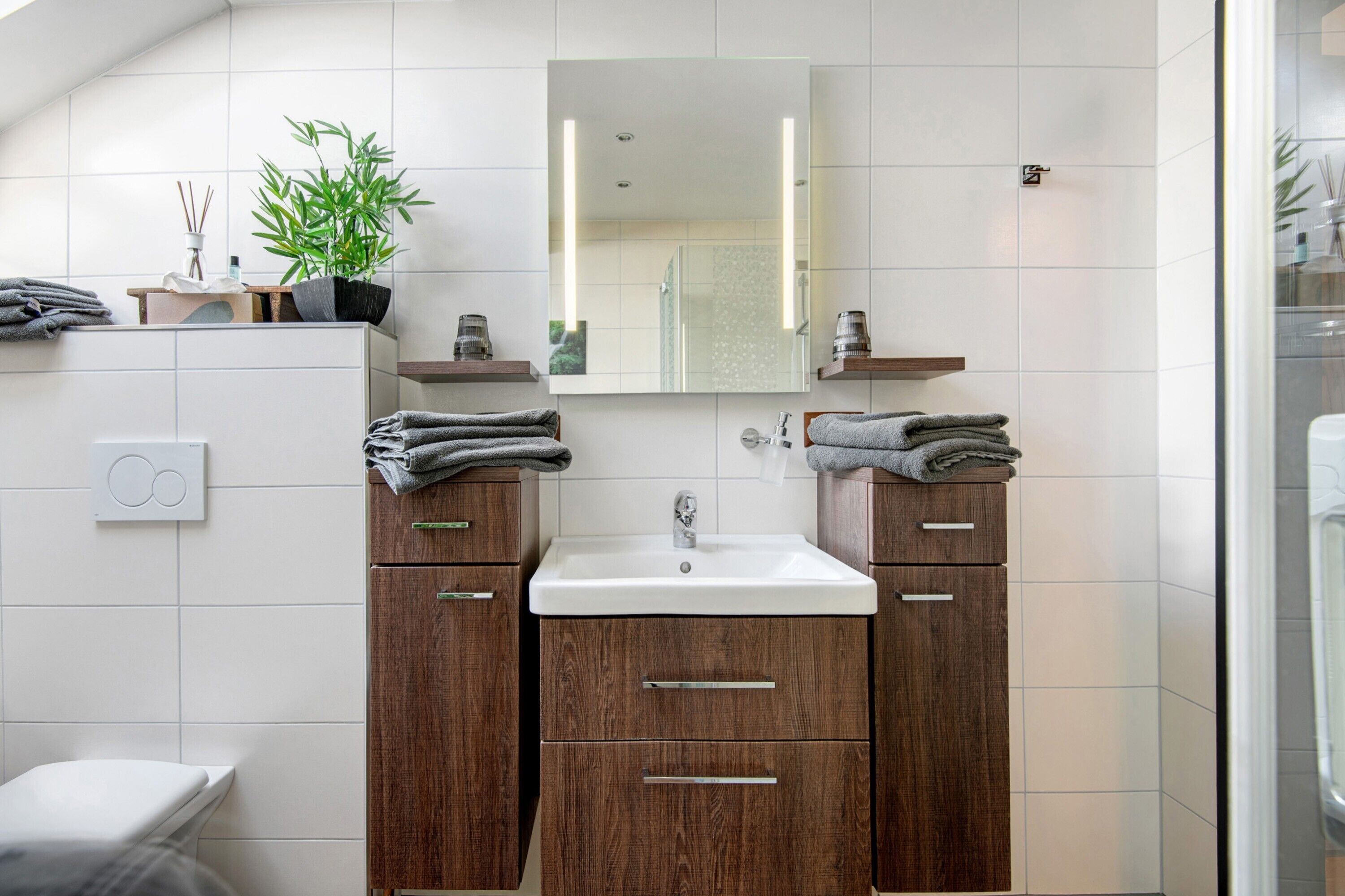 Un baño moderno con un lavabo blanco, armarios de madera, un espejo y un inodoro.