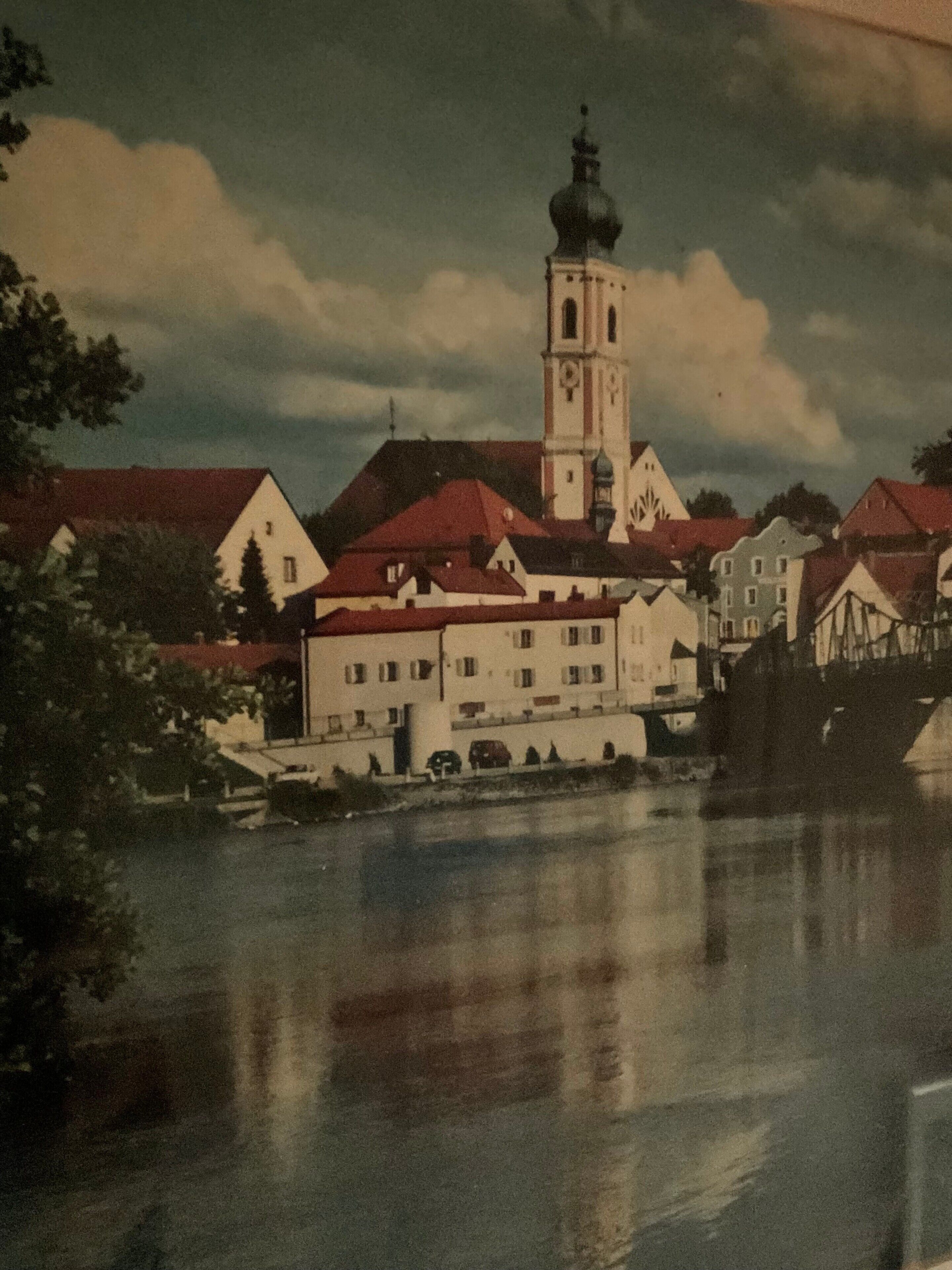Ein historisches Gebäude mit einem markanten Turm, ein Fluss im Vordergrund und eine Brücke im Hintergrund.