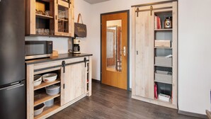 Een keuken met houten kastjes, een koelkast, een magnetron en een schuifdeur naar een andere kamer.