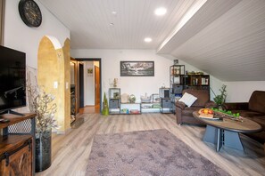 A living room with a TV, a coffee table, a couch, and a bookshelf.